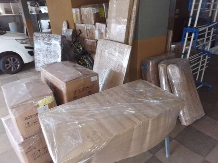 Real on-site stilt parking staging in Chrompet Chennai showing wrapped study table, dimensioned moving cartons, and flat wooden panels ready for truck loading