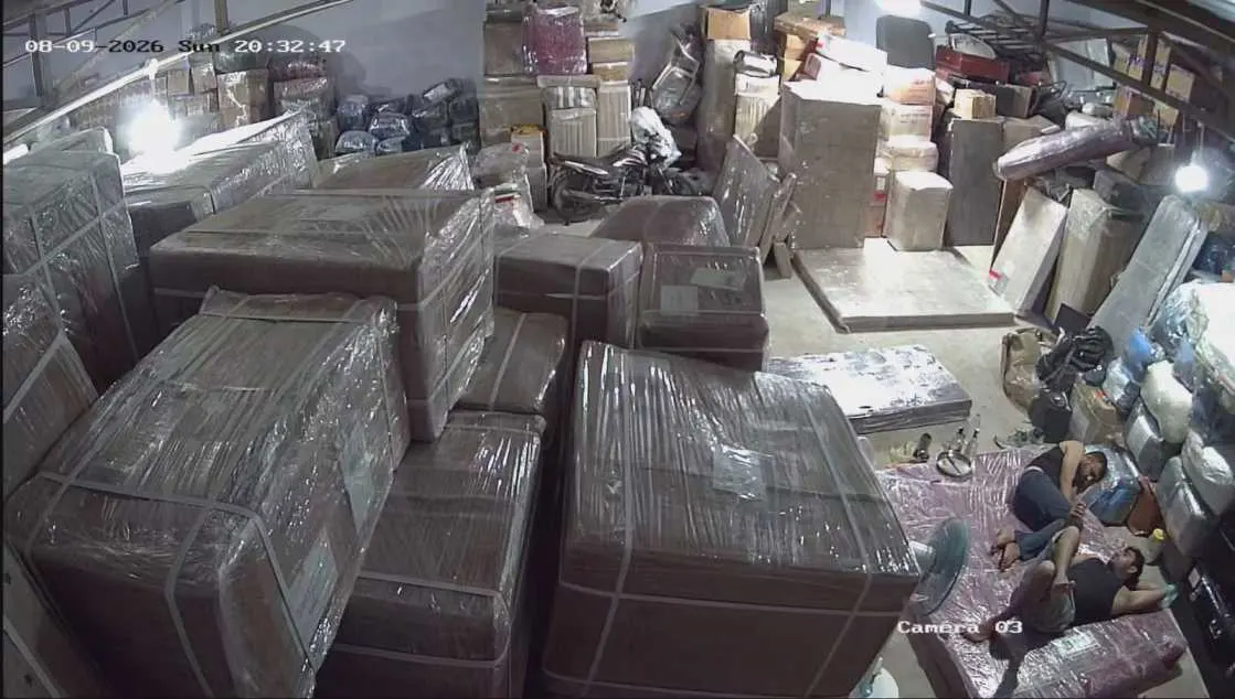 Real CCTV dispatch staging photo of packers and movers Chennai to Bangalore hub showing shrink-wrapped furniture, multi-tier strapped cartons, and bike storage